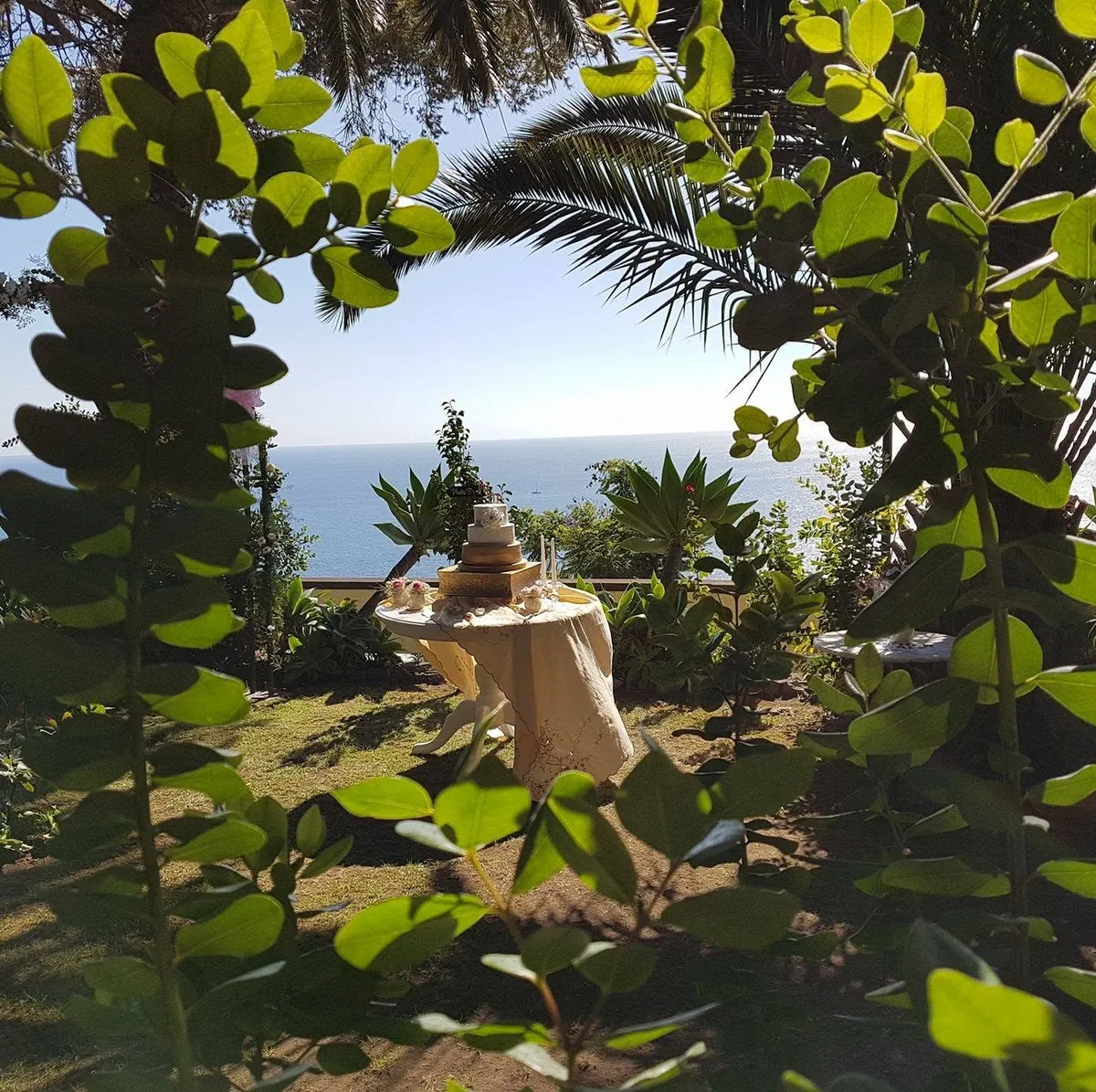 O mar visto entre as árvores do jardim, com uma mesa posta à sombra